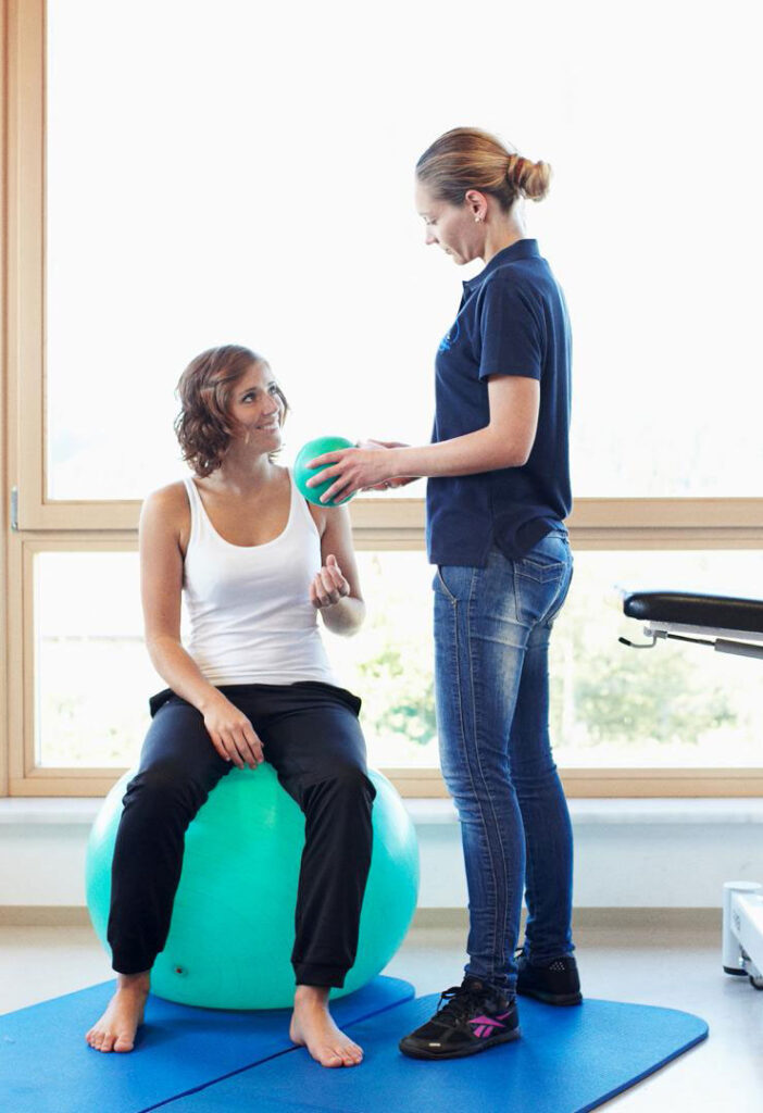 Physiotherapeutin behandelt eine Patientin auf dem Gymnastikball